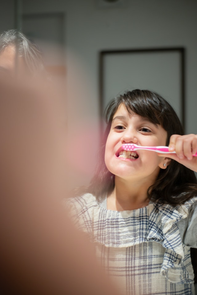 young girl with black hair and plaid shirt practicing her dental hygiene routine by brushing her teeth