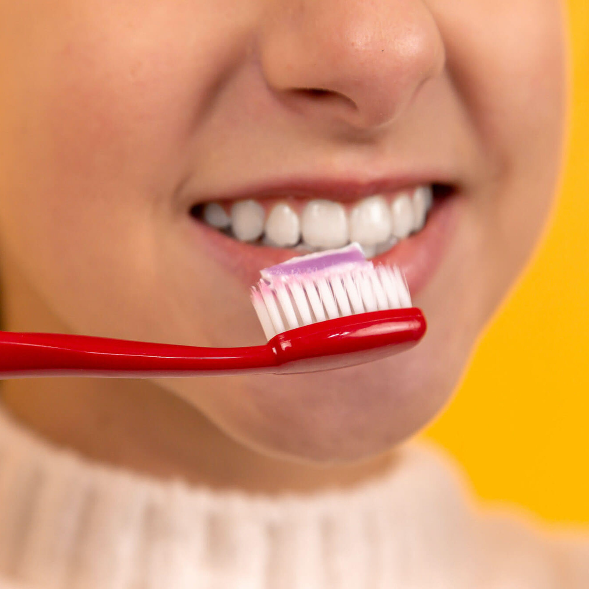 person brushing their teeth with red tooth brush and toothpaste